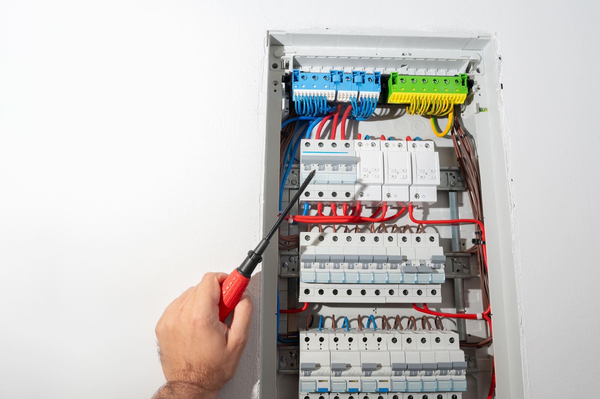 Elektriker med skruvmejsel vid en modern elcentral med automatsäkringar på DIN-skena